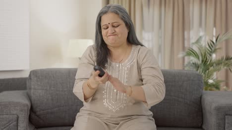 una anciana india enojada tratando de arreglar el control remoto de la tv