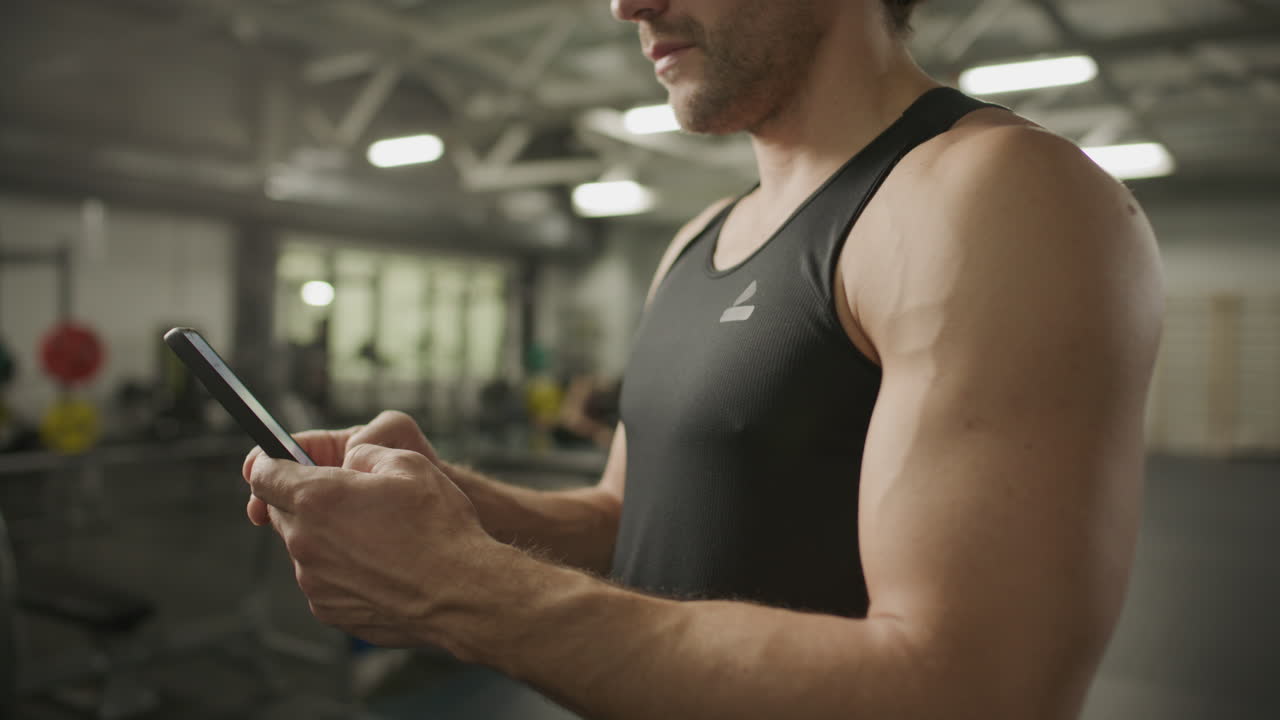 Close-Up of Athletic Man with Muscular Arms Using Mobile Phone in Gym