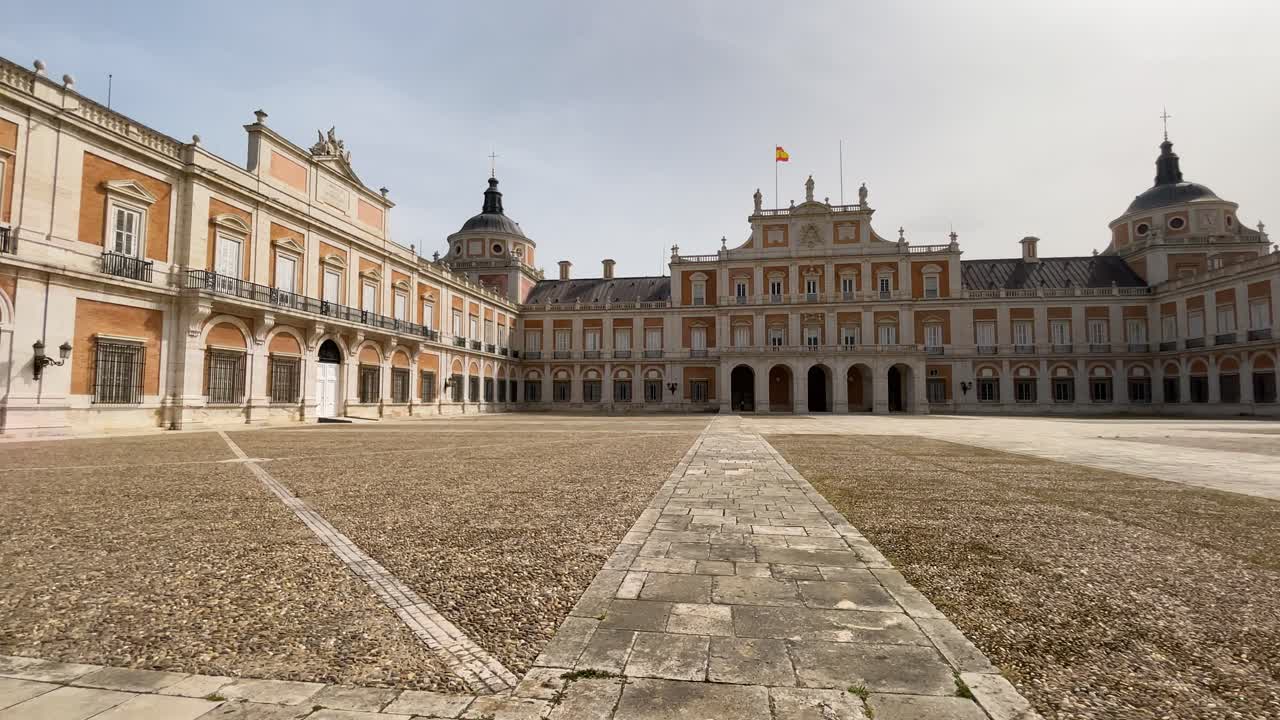 película del patio de armas del palacio real de aranjuez donde tenemos una vista del cuerpo central y las torres laterales de estilo neoclásico caracterizadas por su diseño simétrico y ordenado.