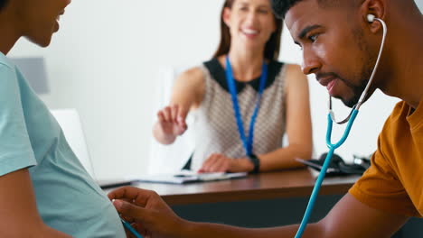 Man-Listening-With-Stethoscope-As-Pregnant-Couple-Have-Appointment-With-Female-Doctor-Or-GP-In-Office