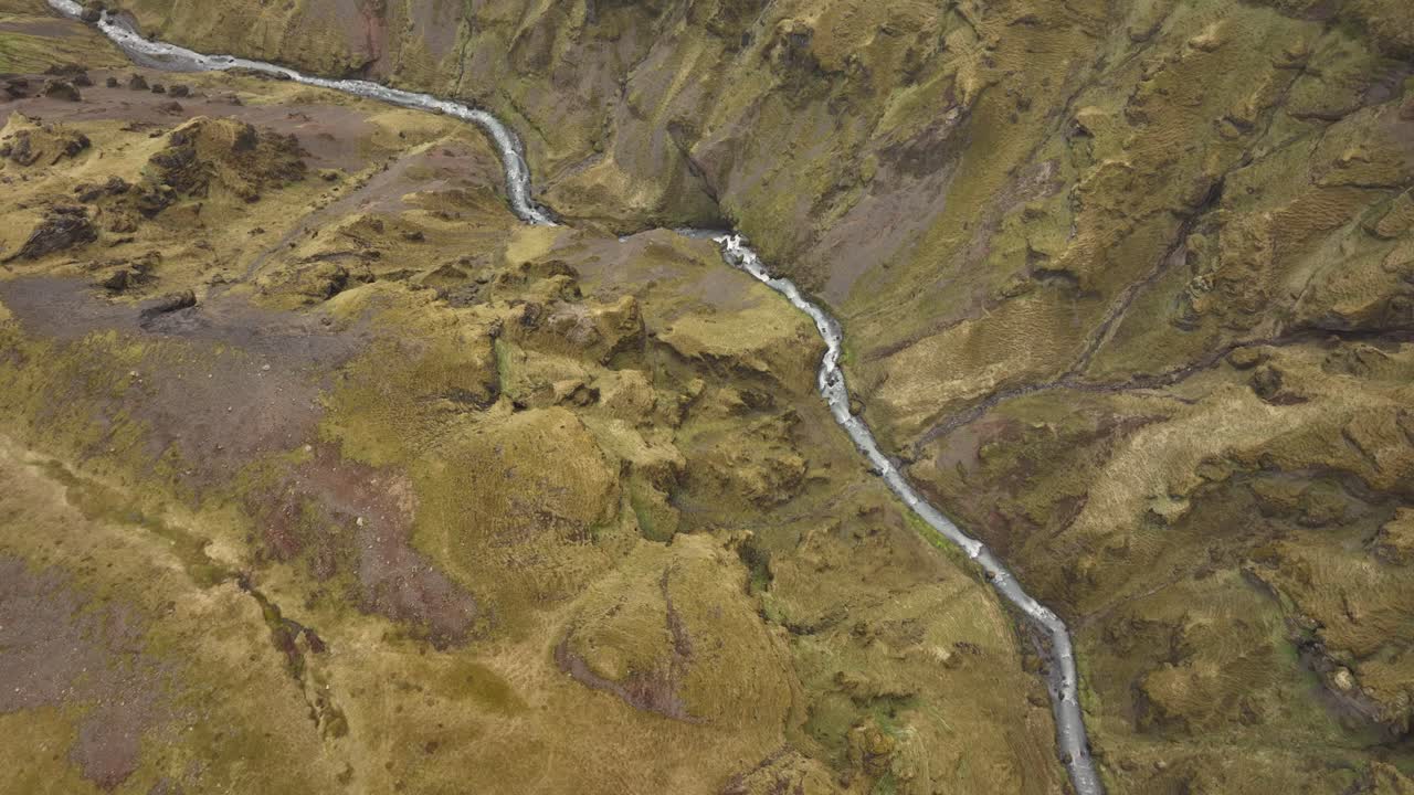 Aerial shot of a winding river carving through a steep, rugged canyon in Brókarjökull, Iceland, with moss-covered cliffs and earthy textures