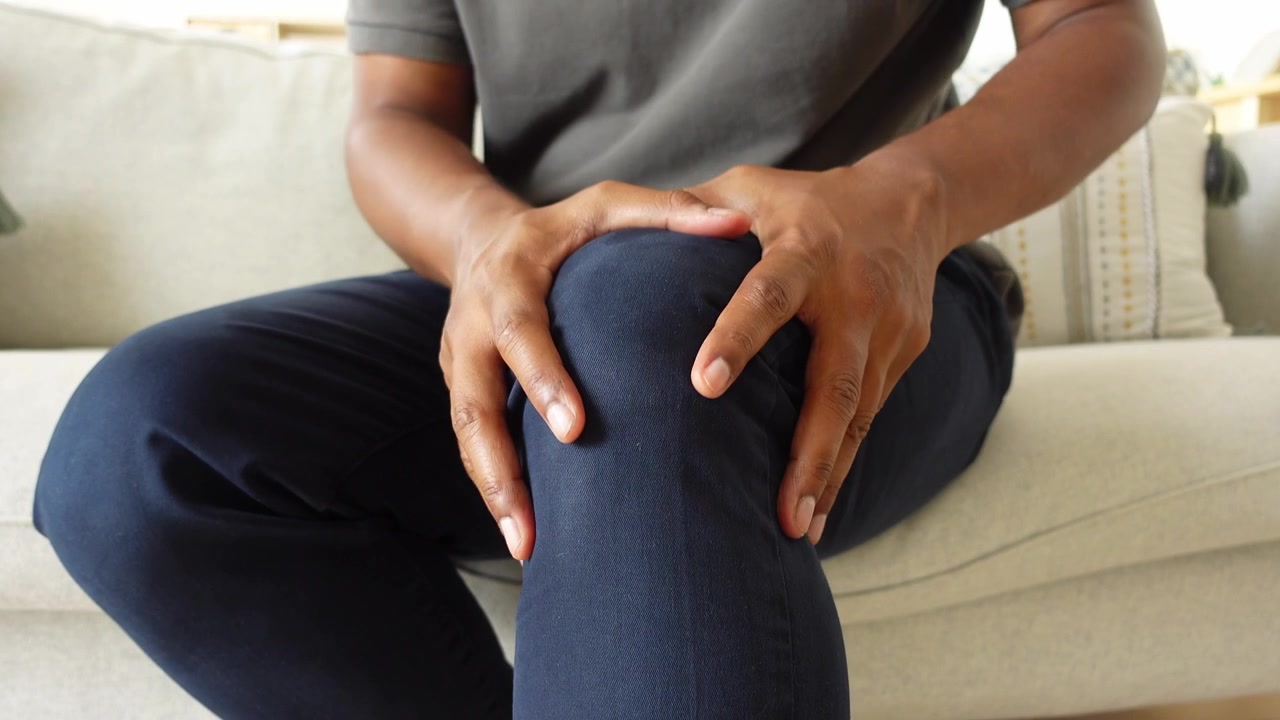 Person Suffering From Knee Pain While Sitting on Sofa