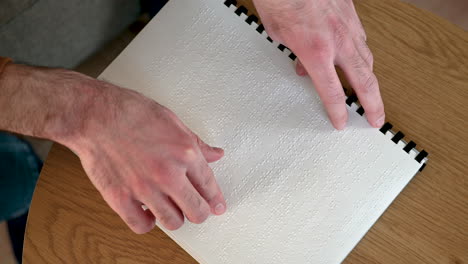 vista superior de un hombre irreconocible leyendo un libro en braille en casa