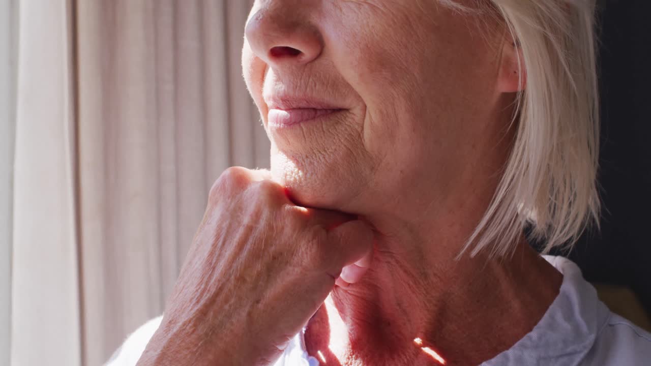 feliz mujer caucásica mayor de pie en el dormitorio, mirando a través de la ventana