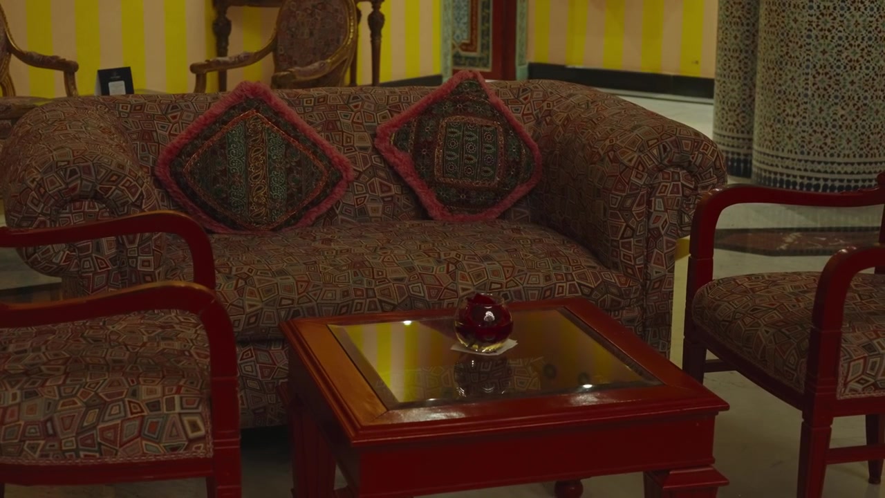 Prunkvolles marokkanisches Wohnzimmer mit gemustertem Sofa, roten Holzstühlen, Couchtisch und gestreifter gelber Wand.