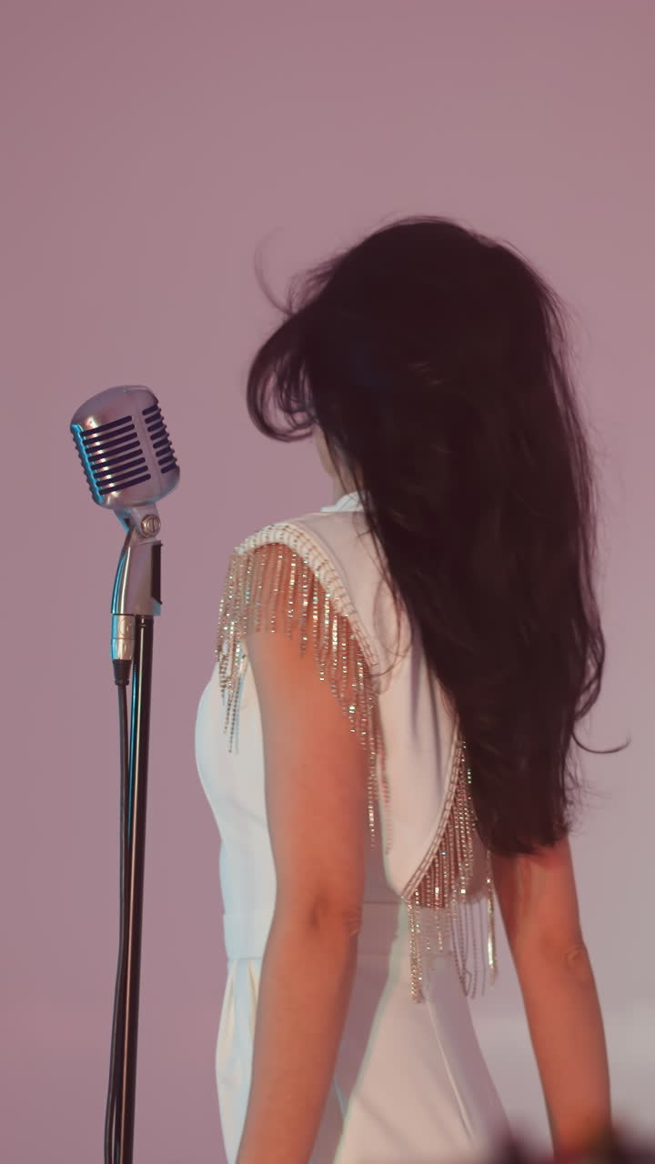 una cantante femenina en un vestido blanco actúa frente a un fondo blanco, moviendo su cabello a la izquierda y a la derecha