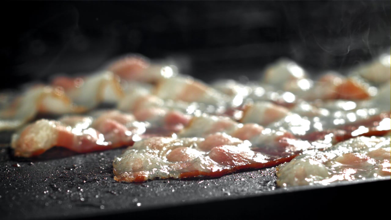 Primo piano di pancetta che frigge e sfrigola su una padella calda