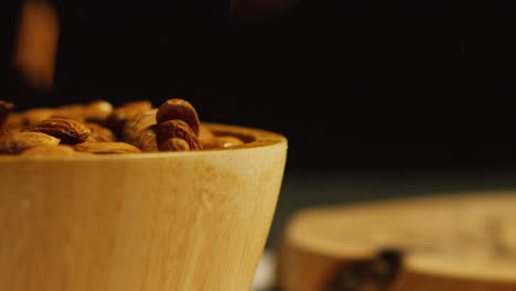 close up shot of almonds dropping into wooden bowl against black studio background shot in slow motion