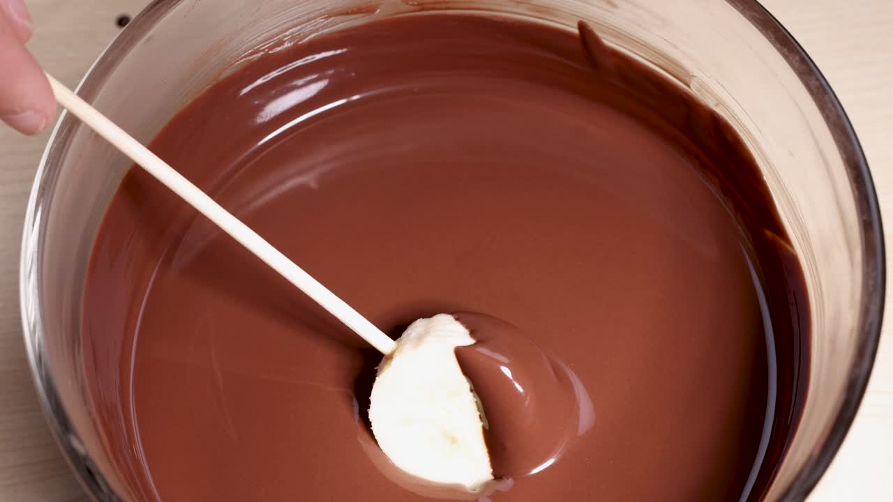 una rebanada de plátano sumergida en chocolate derretido suave con un pinchazo