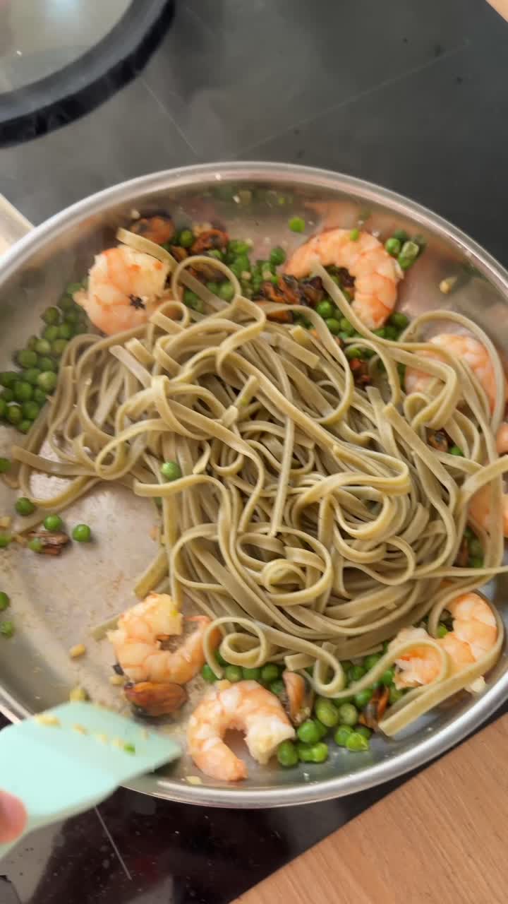 Mescolando pasta fresca con gamberi, piselli e cozze in una padella