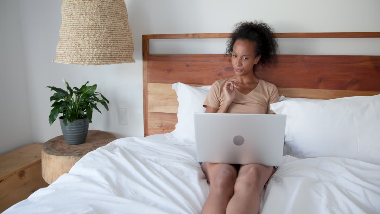 Smiling woman using laptop on bed at home, enjoying relaxed work environment