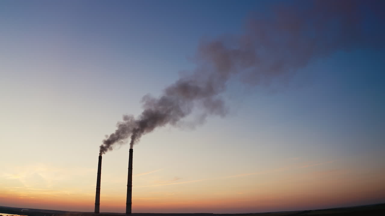 Pollution of the environment.Toxic smoke going from two pipes of a factory on the evening sky background at sunset.