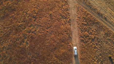 Auto-Fährt-Zur-Goldenen-Stunde-Durch-Unbefestigte-Straße-Mit-Getrocknetem-Gras