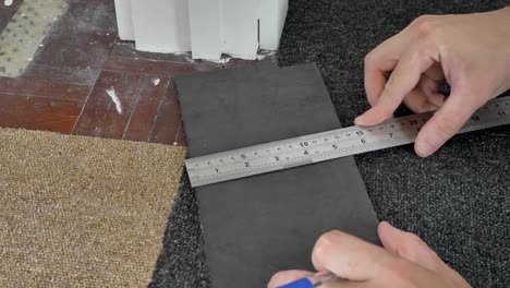 usando pluma y regla para marcar el corte a lo largo de la baldosa de la alfombra