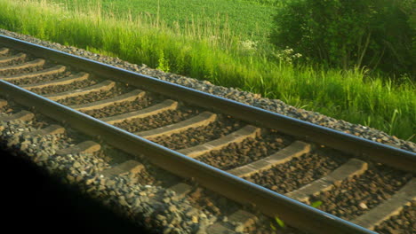 close-up of train tracks through train window on a sunny day, lush green grass in background