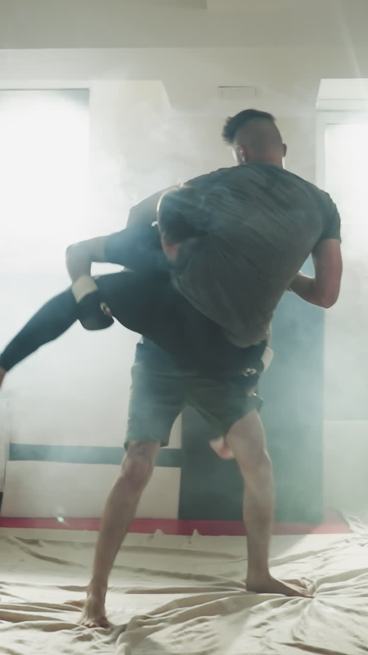 un chico levanta y lanza a su compañero en el piso del club deportivo. un joven ataca a un amigo que hace ejercicio durante el sparring en un gimnasio con niebla en cámara lenta. entrenamiento de artes marciales