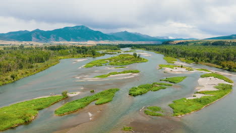 aerial view of a wide river with multiple channels and lush green banks against a mountainous backdrop