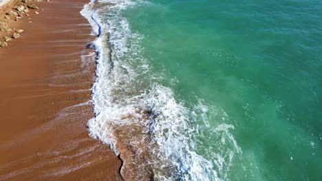 Aerial-view-of-deep-blue-ocean-waves-hitting-the-walking-path-in-between-the-fortress-and-the-city-of-Cadiz,-Spain