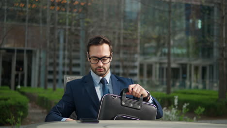 Businessman-opens-a-briefcase-outdoors,-sitting-in-a-park
