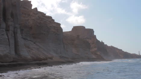 una playa de arena negra en santorini, grecia, rodeada de formaciones de acantilados volcánicos blancos.