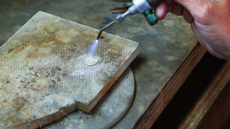 close-up of craftswoman blowing a torch to melt metal