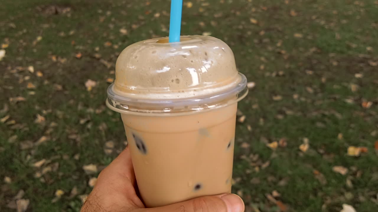 Primo piano di un uomo che tiene in mano un bicchiere di latte macchiato freddo in un parco