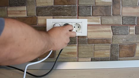 Wide-frame-of-triple-power-wall-socket-being-plugged-and-unplugged-with-appliances,-by-a-man's-hand