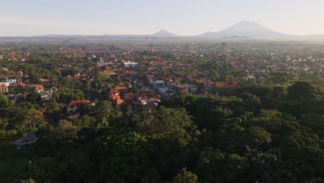 Filmischer-Sonnenaufgangsblick-Auf-Die-Stadt-Ubud,-Die-Für-Ihr-Traditionelles-Kunsthandwerk-Berühmt-Ist,-Mit-Dem-Vulkan-Agung-Im-Hintergrund-Und-Dem-Affenwald-Im-Vordergrund