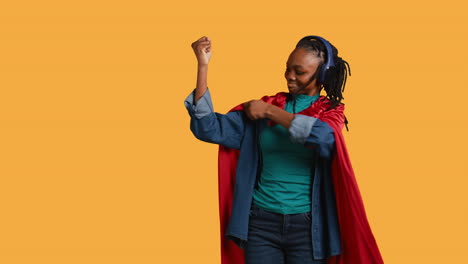 Woman-wearing-cloak-posing-as-hero-in-costume-kissing-biceps,-studio-background