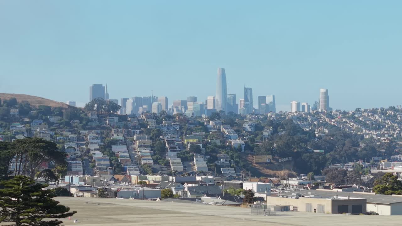Bernal Heights' compact grid unfurls beneath soft skies, framed by trees and the skyline in the distance.