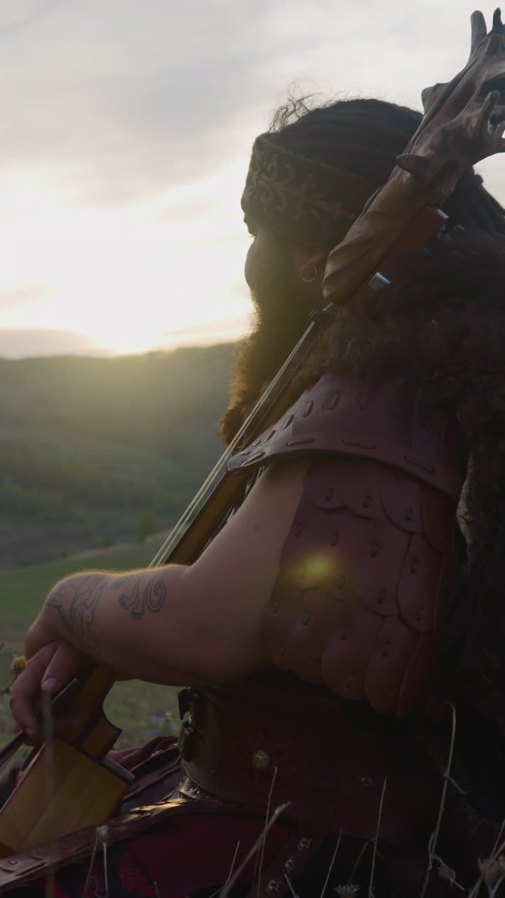 Resting man in shaman clothes sits leaning on ikili in mountain valley at sunrise. Participant of folk rock band. Altai culture and traditions