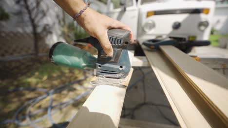 man using electric sander, sanding wood outdoors, wood work, slow motion