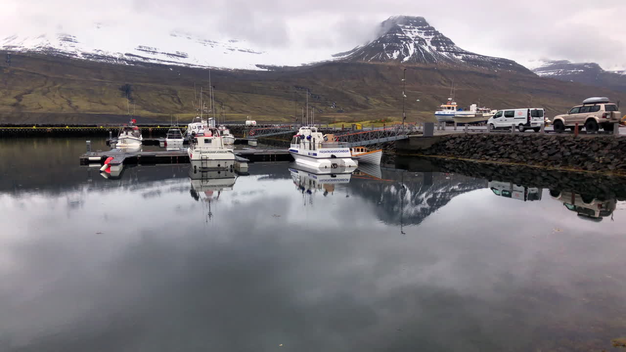 Boats moored in a small harbor at the foot of the mountains covered by snow and clouds