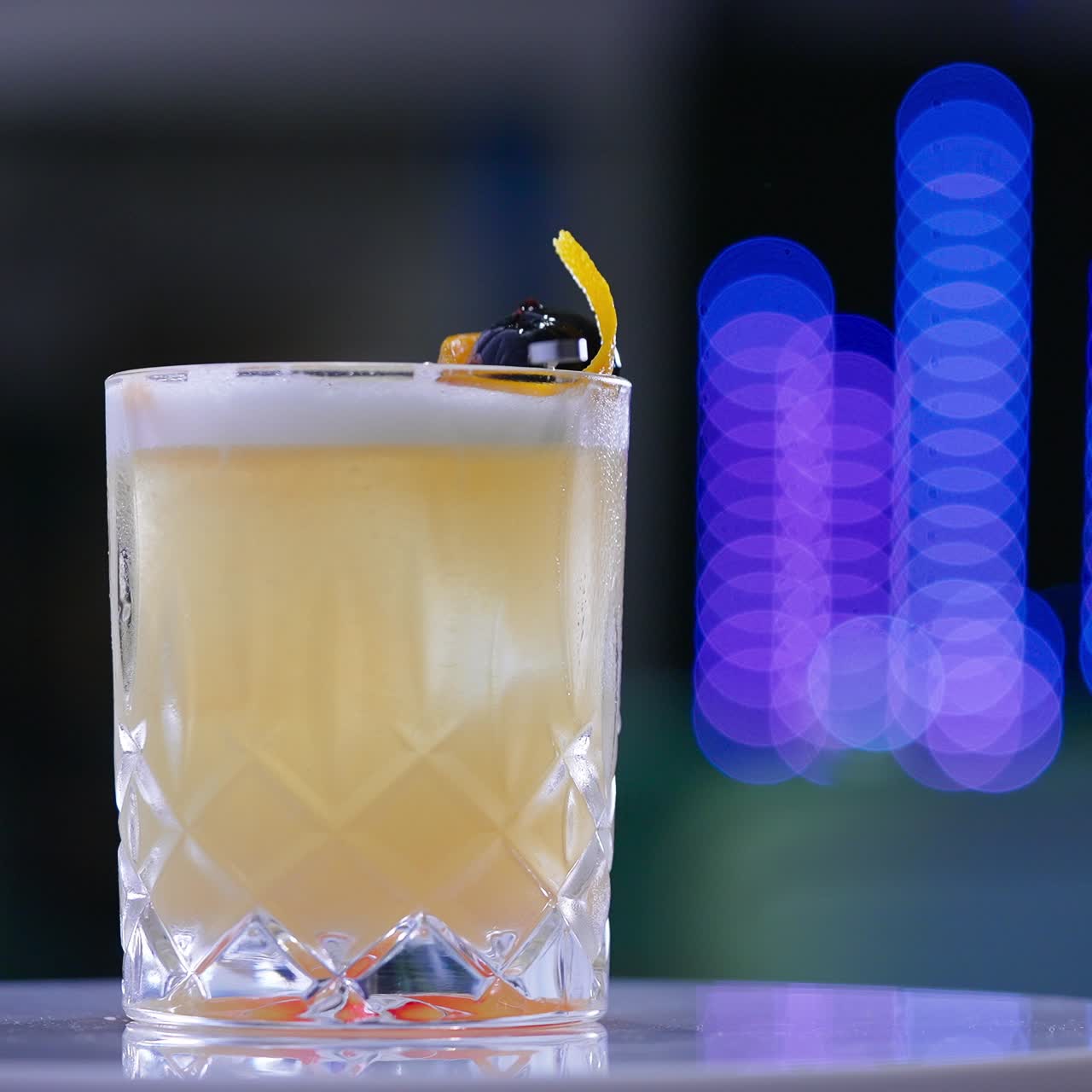 Beautifully decorated cocktail in the wide glass on the rotating white table. Beverage served in the bar. Close up. Blurred backdrop