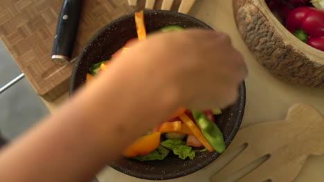 close up of female hands placing green pepper in salad bowl