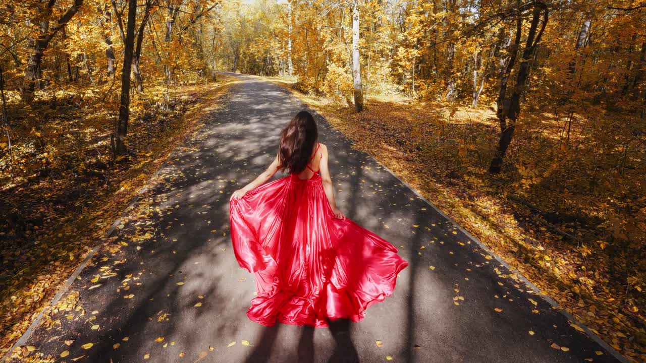 A Woman in a Flowing Red Dress Walks Gracefully Along a Serene Autumn Path Surrounded by Vibrant Golden Leaves, Capturing the Essence of Fall's Beauty and Tranquility