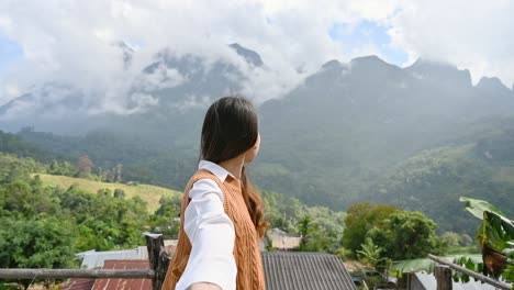 asian woman holding hands of her boyfriend while enjoying the mountain view on the hill at viewpoint in chiang dao