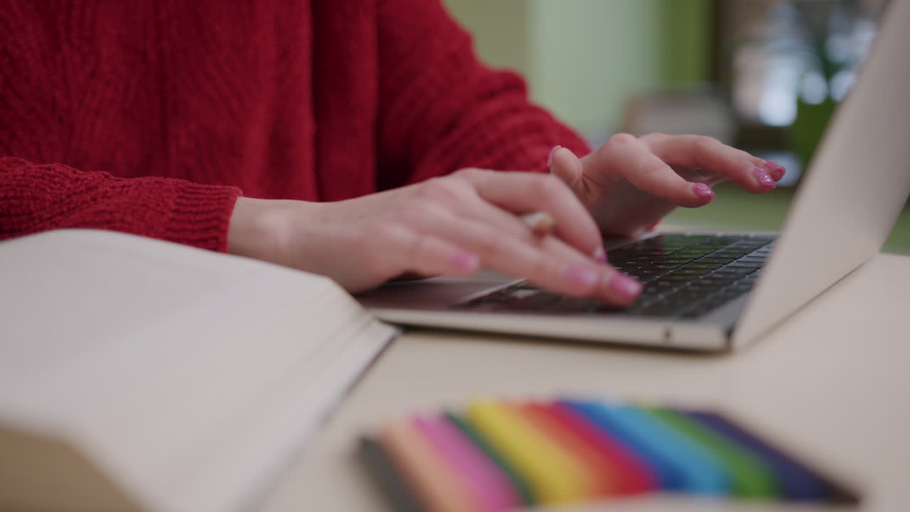 primer plano de las manos de una chica que estudia pasando las páginas de un libro y usando una laptop