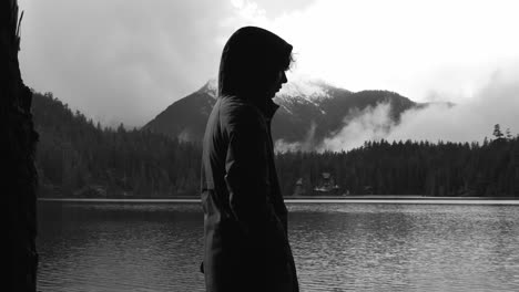 Person-In-Hoody-Jacket-Standing-In-A-Lakeshore-Against-Overcast-Sky