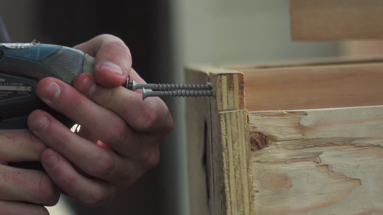 primer plano, de las manos de los trabajadores de la construcción perforando dos tornillos en madera con taladro eléctrico
