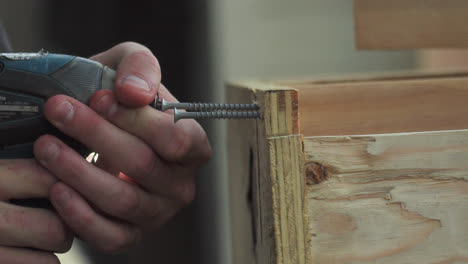 primer plano, de las manos de los trabajadores de la construcción perforando dos tornillos en madera con taladro eléctrico