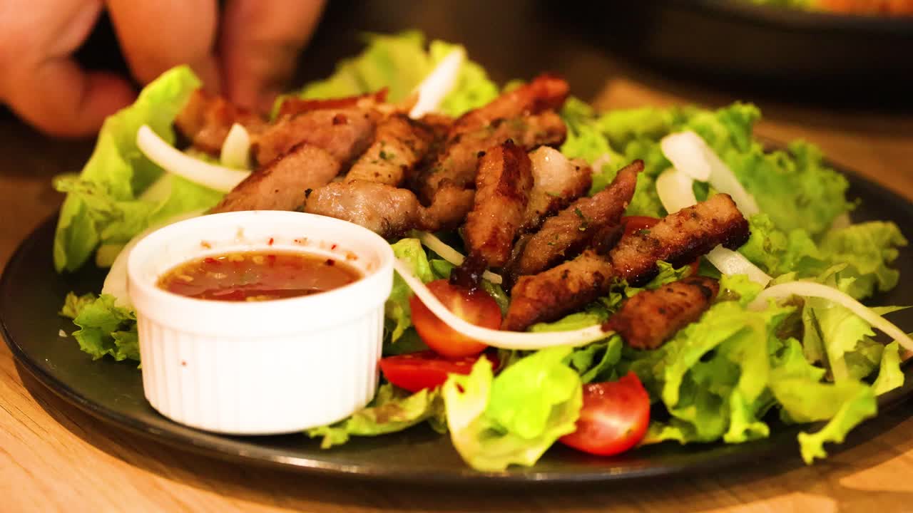manos arreglando ensalada de cerdo a la parrilla con salsa
