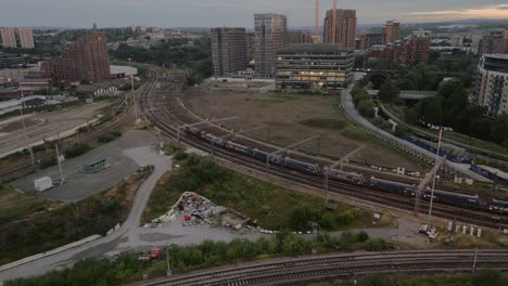 Aerial-Drone-Shot-of-Freight-Train-Leaving-Leeds-City-Centre-Train-Station-at-Sunrise