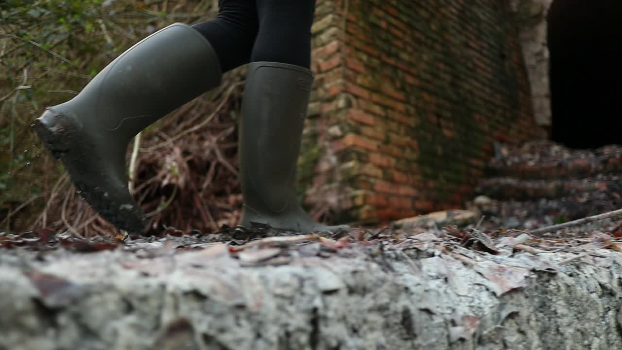 chica camina en el barro de azufre con botas verdes antes de entrar en la vieja mina, toma de cerca