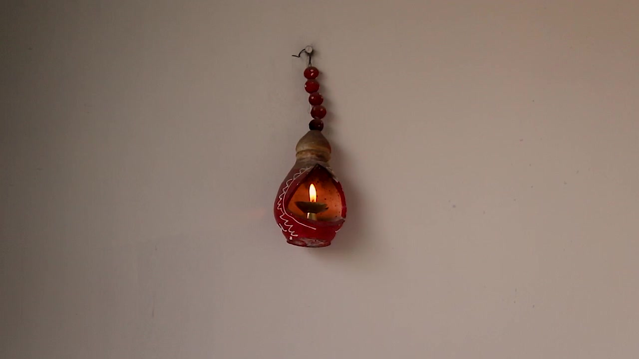 Tradizionale lampada diya sospesa con fiamma luminosa contro una parete pulita. Ideale per Diwali, spiritualità, meditazione, preghiera, cultura indiana, arredamento per la casa e progetti di stile di vita festivo.