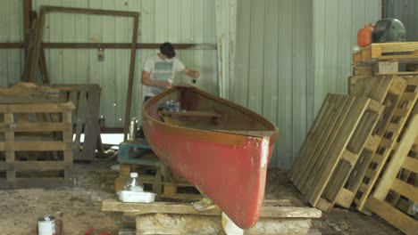 un carpintero barniza la madera de una canoa de fibra de vidrio