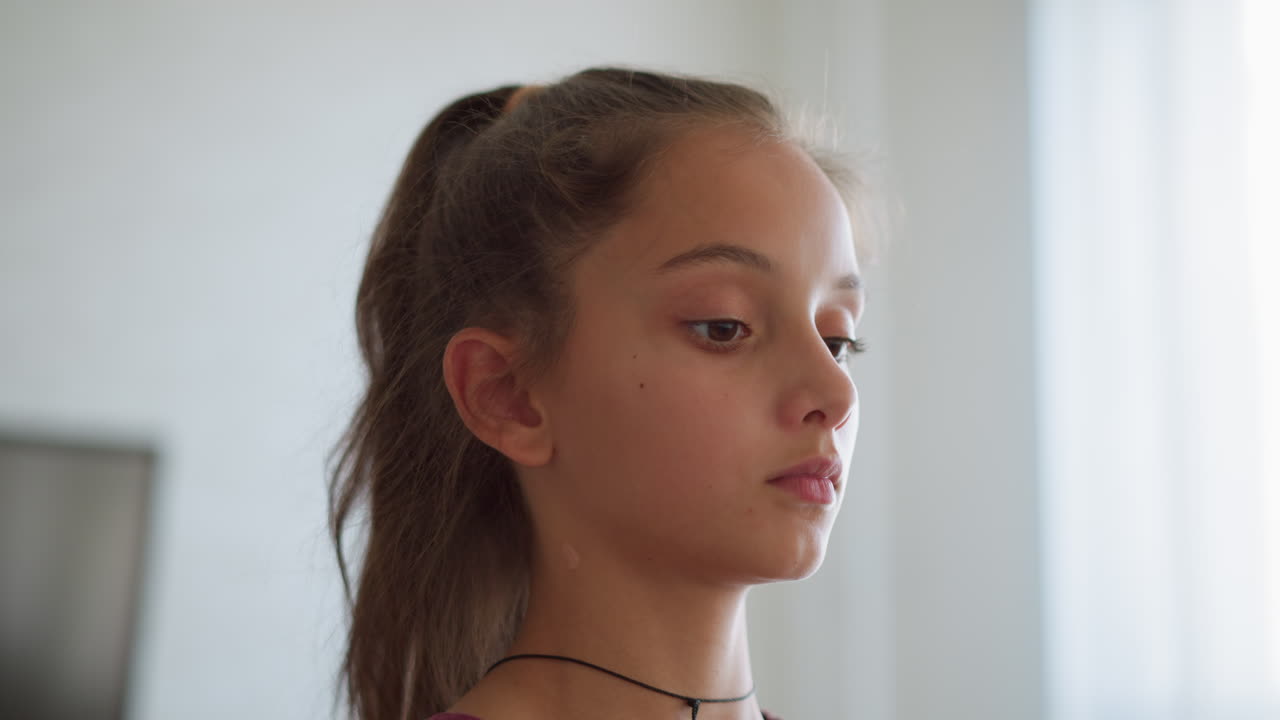 Close-up of focused young girl with rope necklace as she walks, sunlight filtering through window creating a soft, serene atmosphere