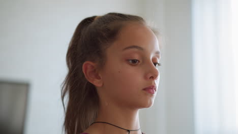 close-up of focused young girl with rope necklace as she walks, sunlight filtering through window creating a soft, serene atmosphere