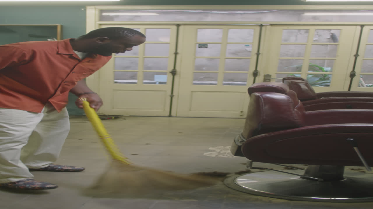 Barber Sweeping Floor with Broom in Barbershop Salon