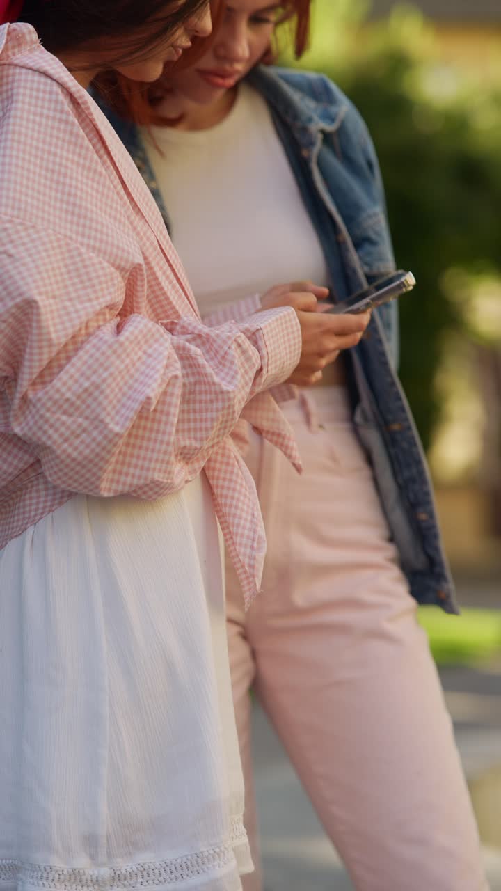 dos mujeres jóvenes usando un teléfono inteligente al aire libre